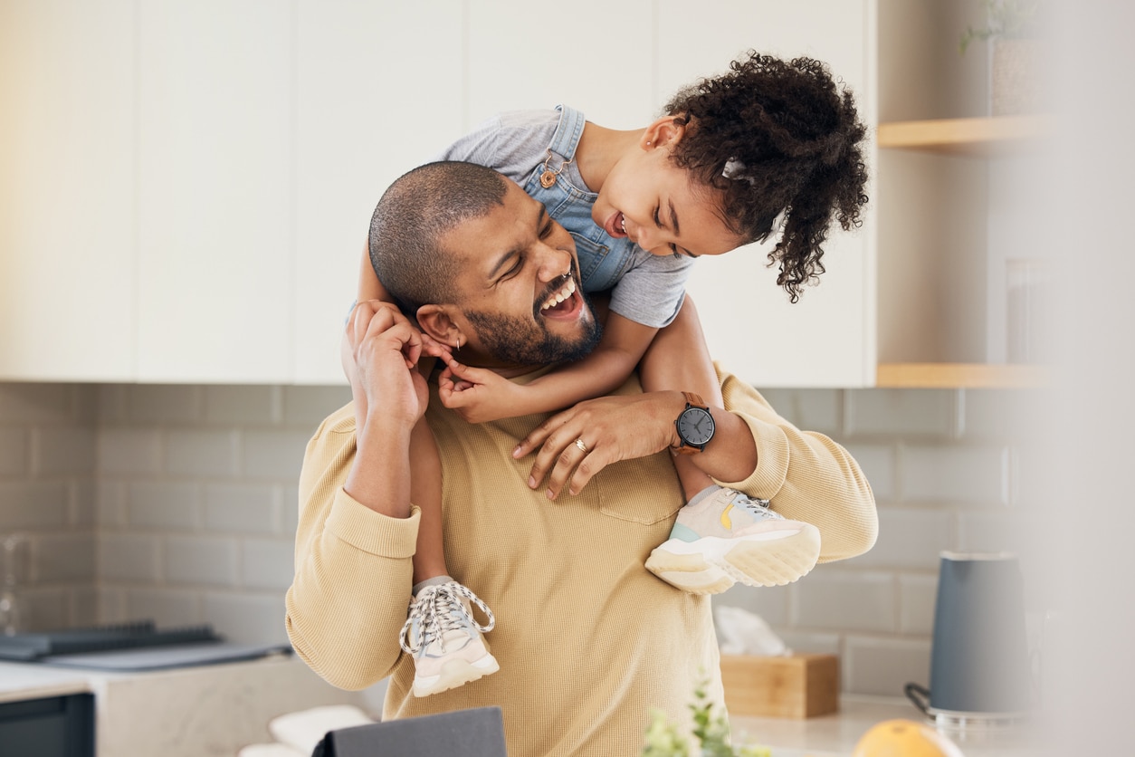 Happy family, hug and father and girl child in a kitchen with piggyback, games and fun, breakfast and laugh at home\. Love, smile and parent with kid embrace, playful and bonding in a house on weekend