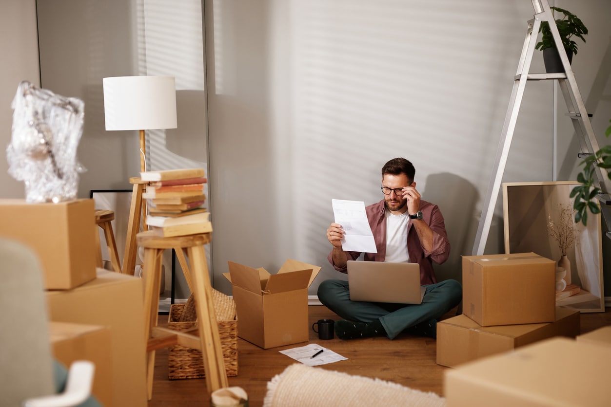 Young man reading documents and working on laptop while moving into new apartment