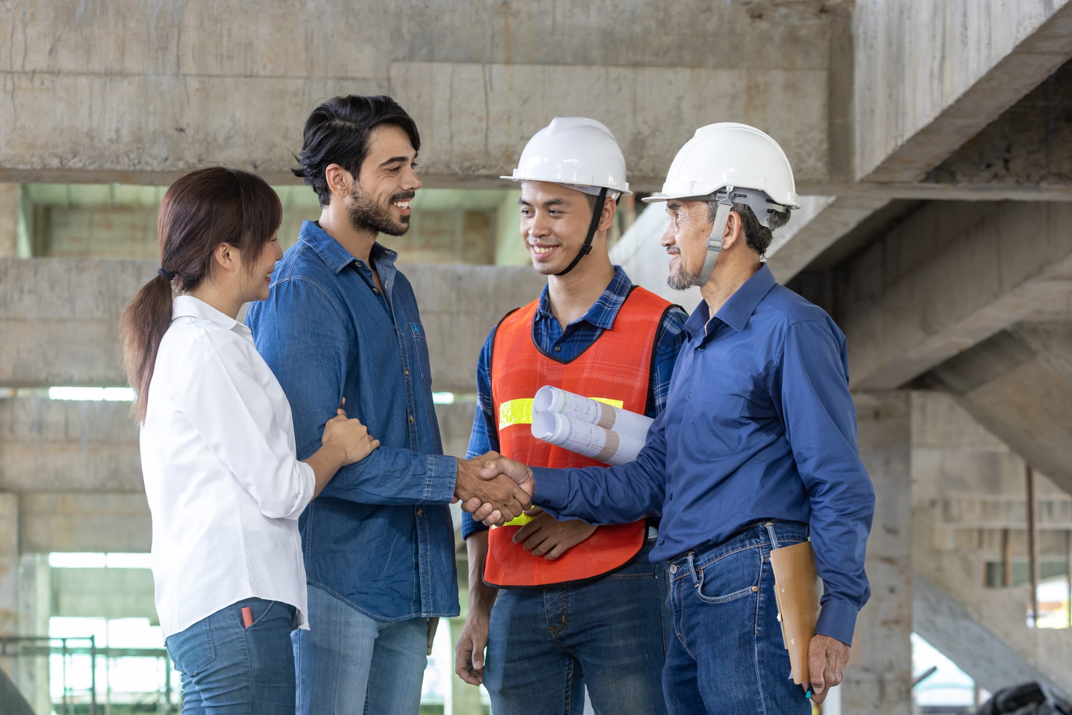 Newly wed couple is handshaking with engineering contractor at the under construction house to inspect building progress and quality control for home ownership and real estate development